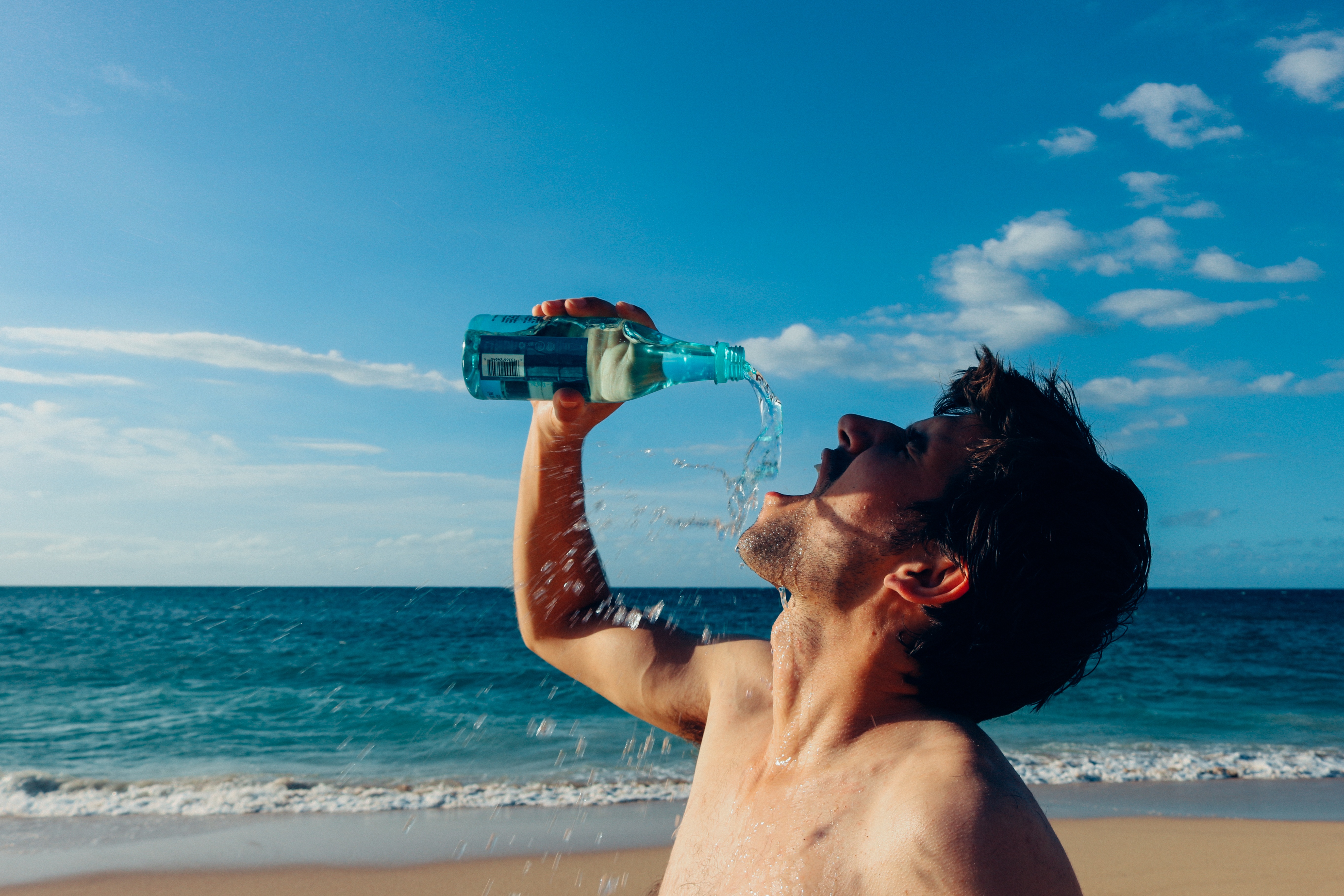 Волнующий воду. Дринкинг Ватер. Алкоголь на пляже. Пьет мужчина воду на пляже.